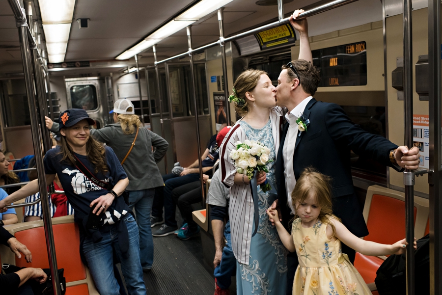 A newly married couple share a kiss as they ride the subway.